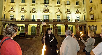 Nachtwächterrundgang Eisenstadt © Ch. Seywerth Ein Mann in historischem Nachtwächterkostüm vor einem Schloss und drei Personen mit Fackeln